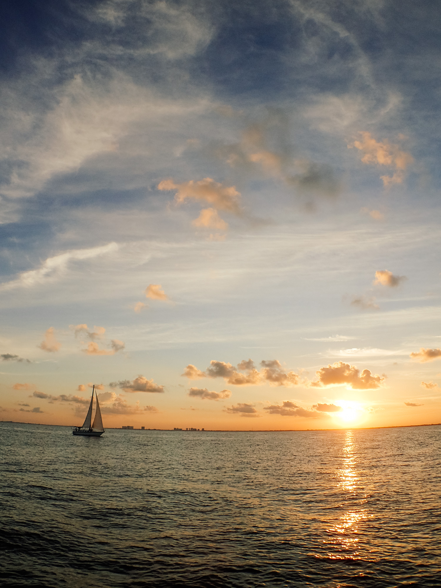 Silhouette of a small sailboat on open water at sunset, glowing orange sun near the horizon